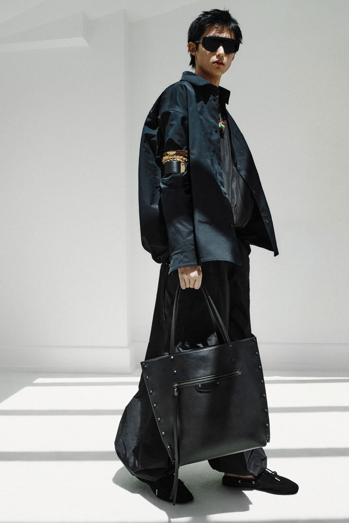 Model in dark shirt, black trousers, sunglasses and black leather tote.