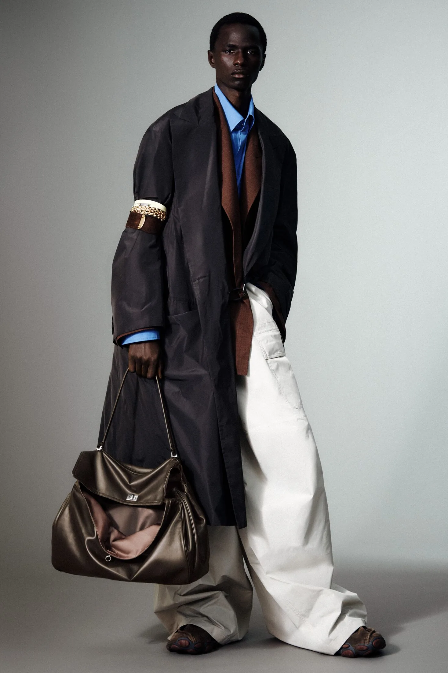 Model in dark coat, blue shirt, white wide-leg trousers and brown leather bag.