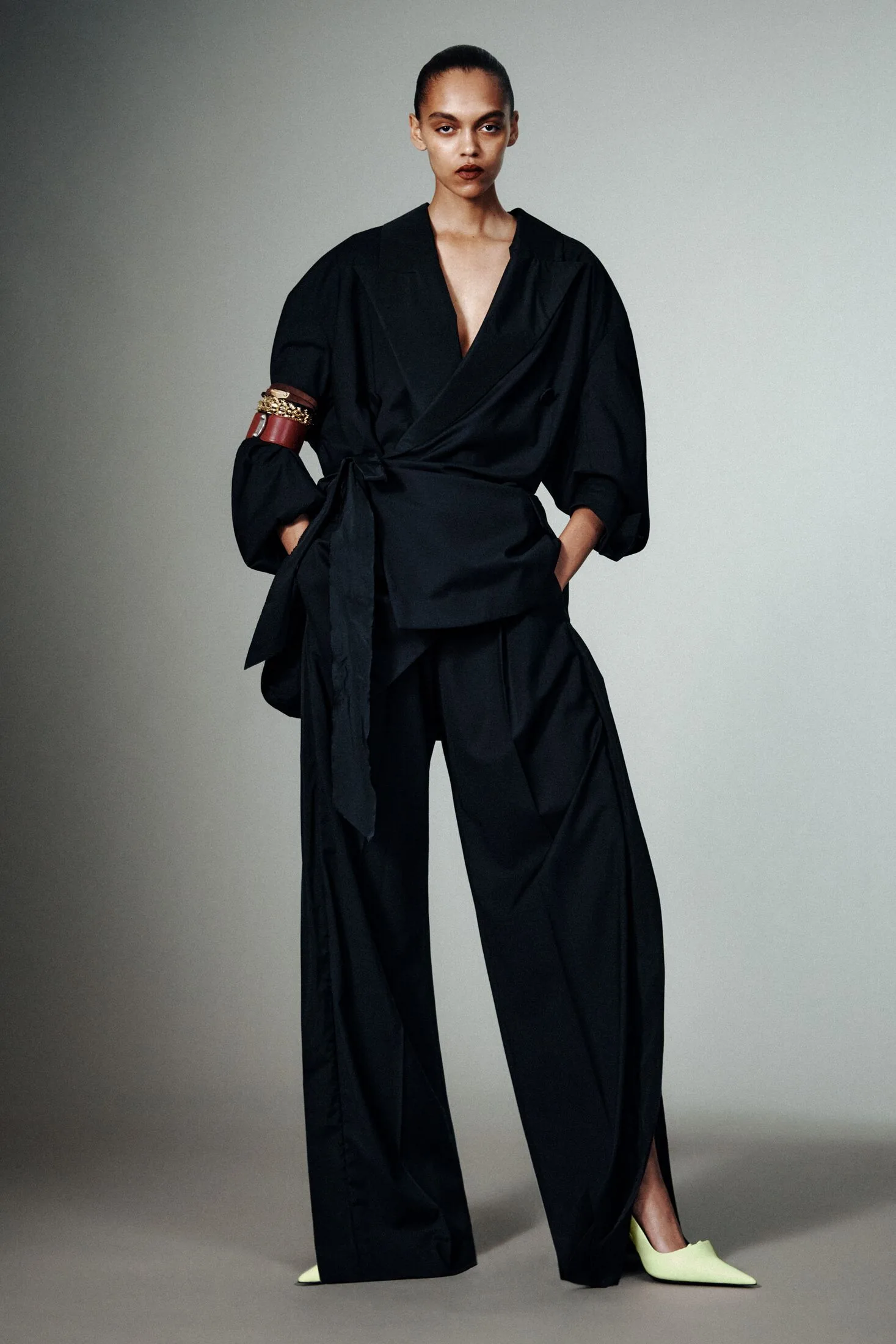 Model in black wrap top, black wide-leg trousers and pale pointed heels.
