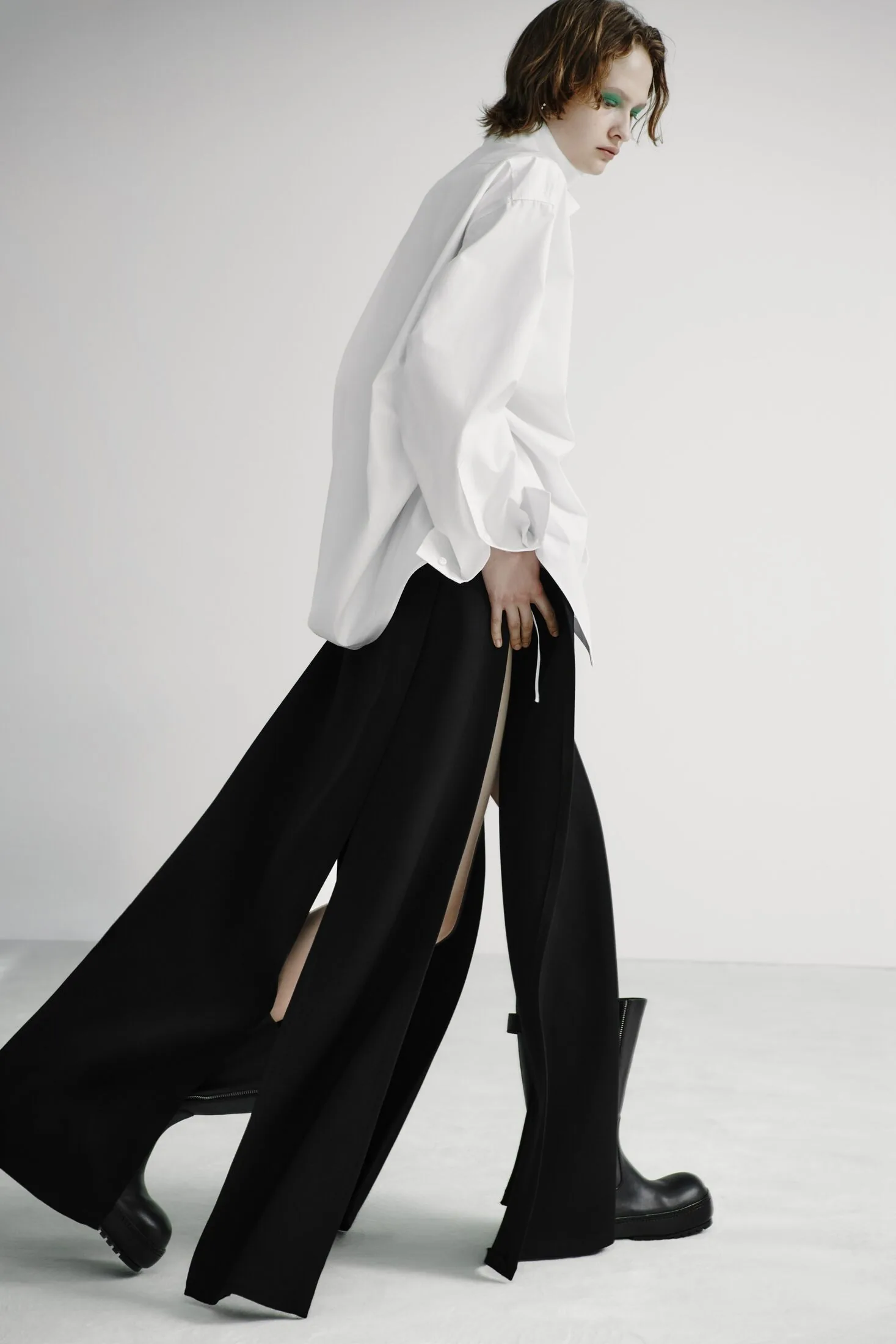 Model in oversized white shirt, black split trousers and black boots.