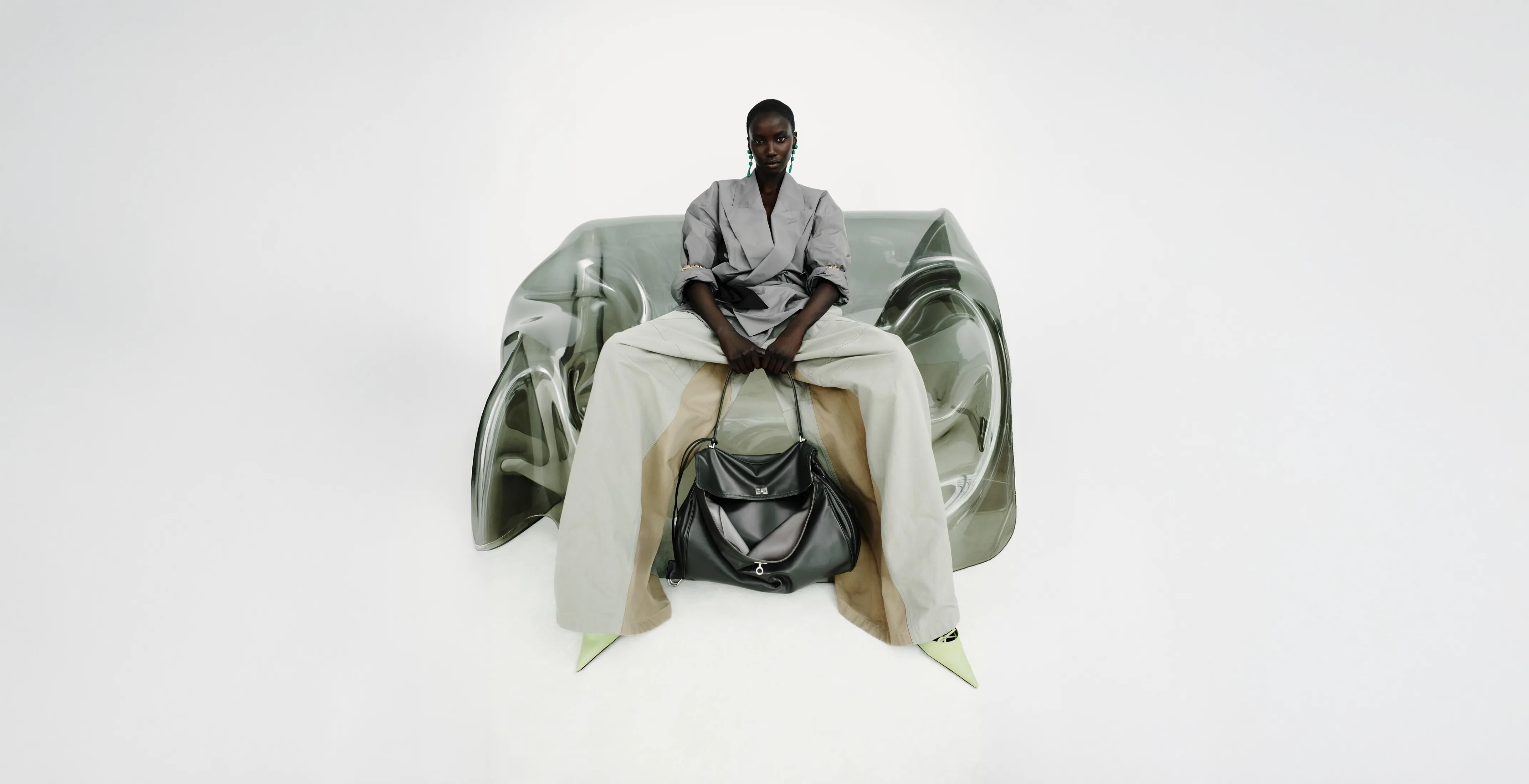 Seated model in grey wrap top, wide pale trousers and black leather bag.